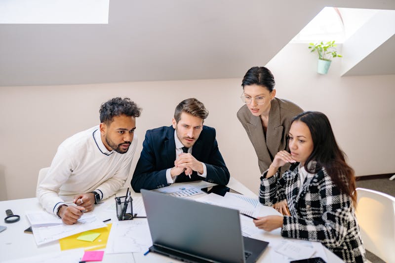 Group of businesspeople collaborating around a laptop screen